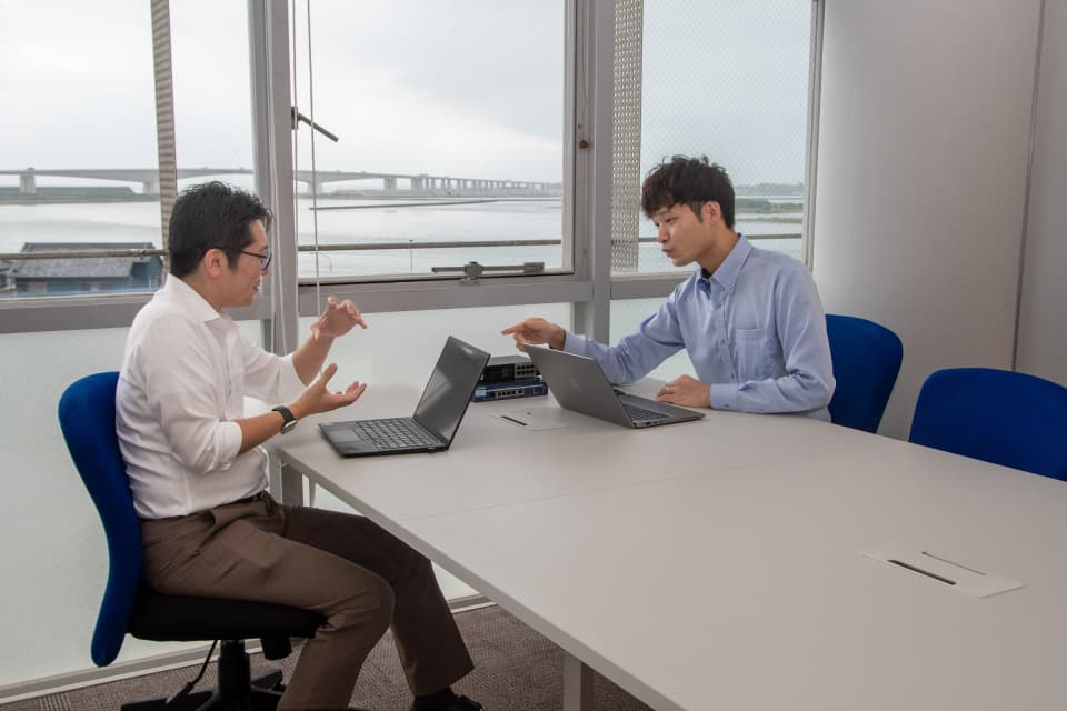 ネットワーク機器を置いたテーブルを挟み、ノートパソコンを前に二人が打ち合わせをしている様子